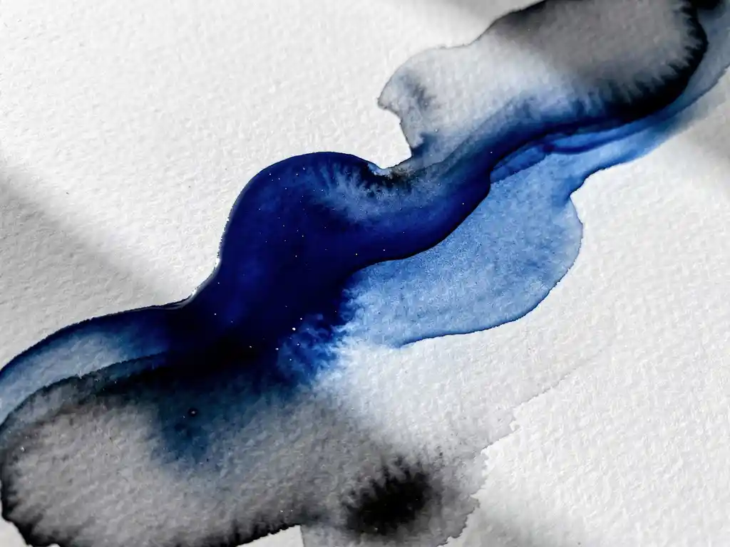 Vloeiende aquarelverf in diep kobaltblauw overgaand in zachte grijstinten op getextureerd aquarelpapier, bovenaanzicht