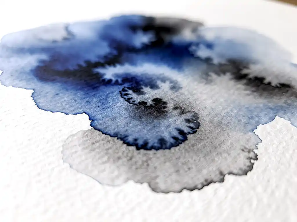 Waterverf in diepblauw en grijs vloeit over wit papier met natuurlijke kleurovergangen en papierstructuur zichtbaar