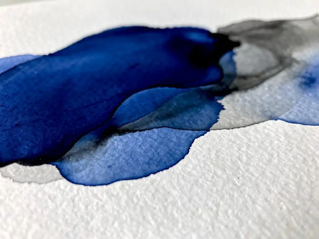 Diepe kobaltblauwe aquarelverf vloeit organisch over wit papier met grijze ondertonen aan de randen