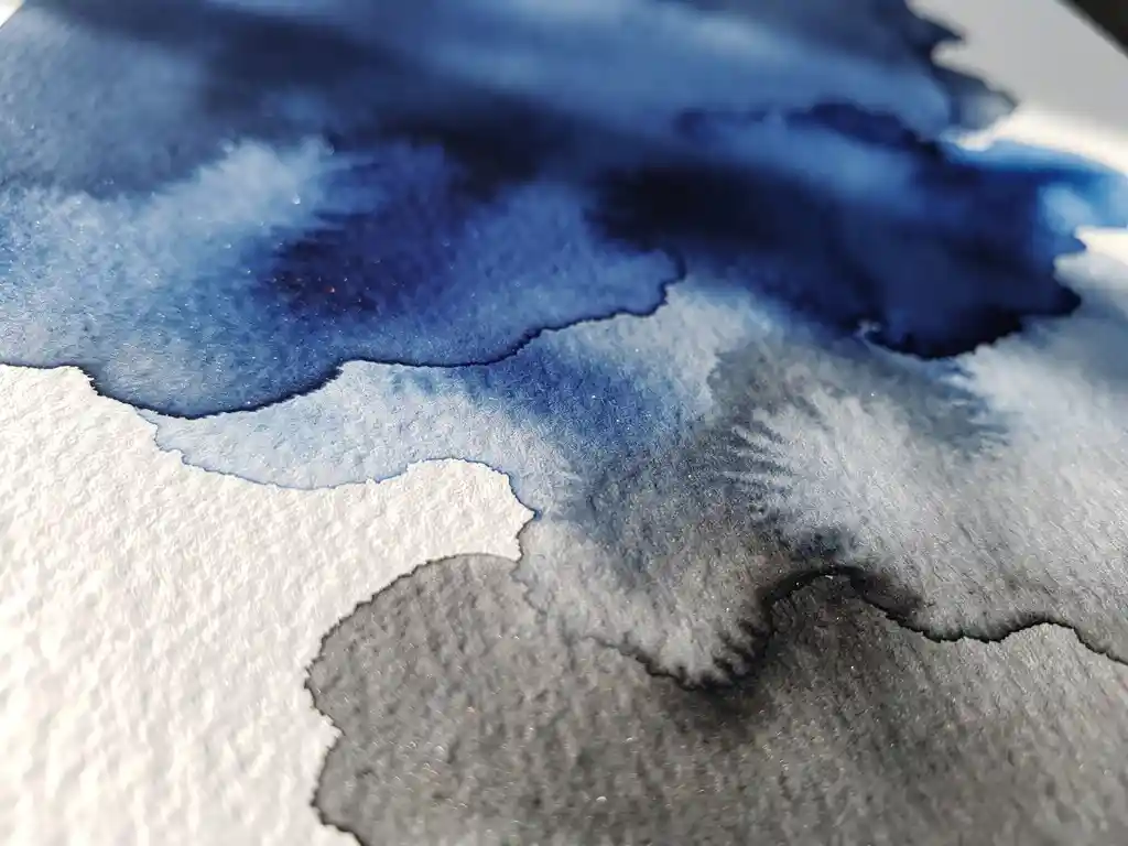 Abstracte aquarelverf in kobaltblauw en houtskoolgrijs vloeit over getextureerd wit papier met natuurlijke kleurovergangen