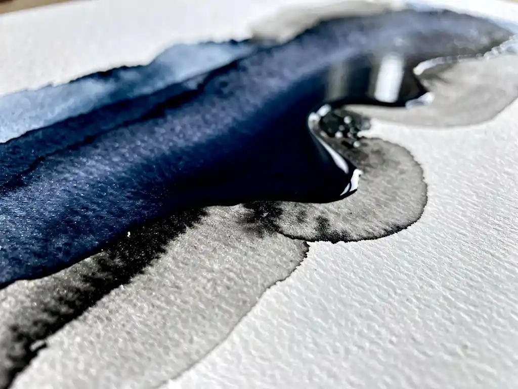 Donkerblauwe aquarelverf vloeit over wit papier met grijze wassen en zwarte accenten, macrofotografie toont papiertextuur