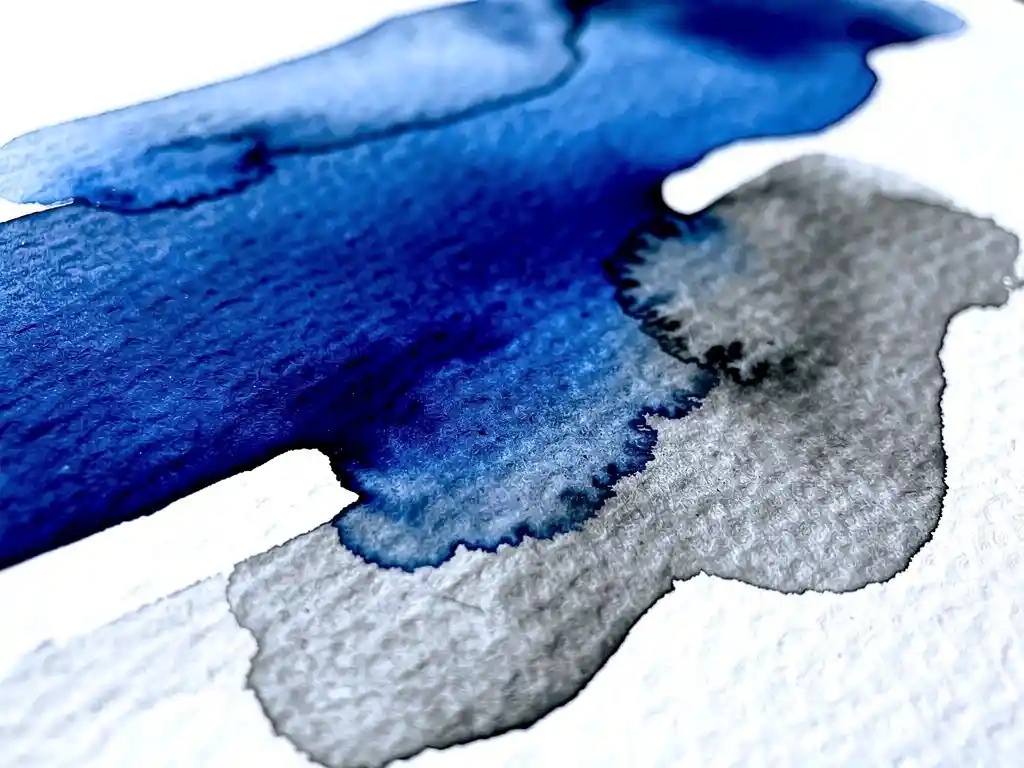 Vloeibare aquarelverf in kobaltblauw en houtskoolgrijs die over getextureerd wit papier vloeit met organische abstracte vormen