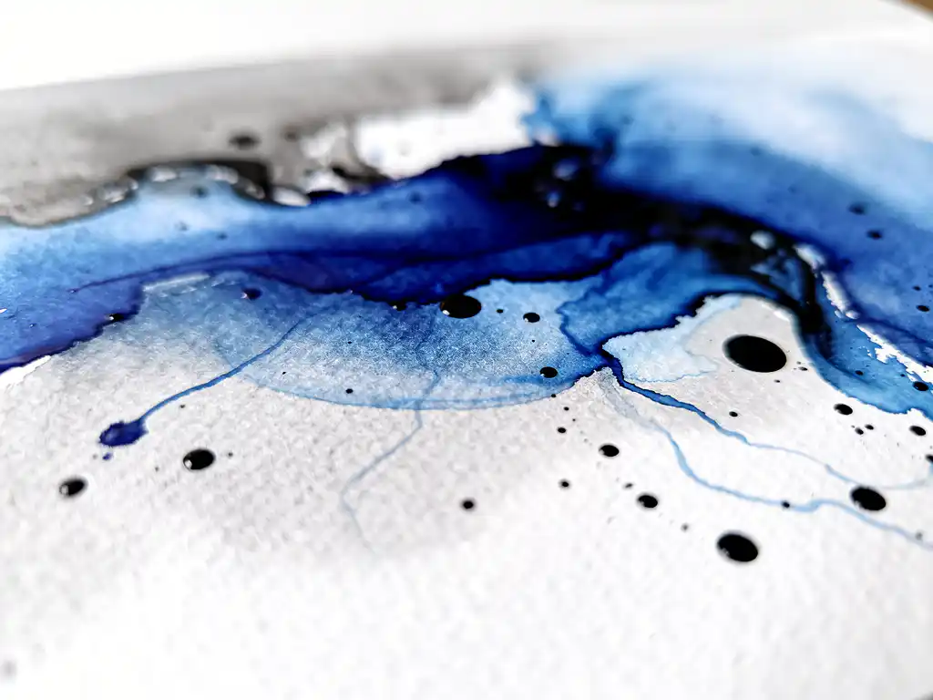 Abstracte aquarel met diepblauwe pigmenten die overvloeien in grijze tinten met zwarte inktdruppels op wit papier