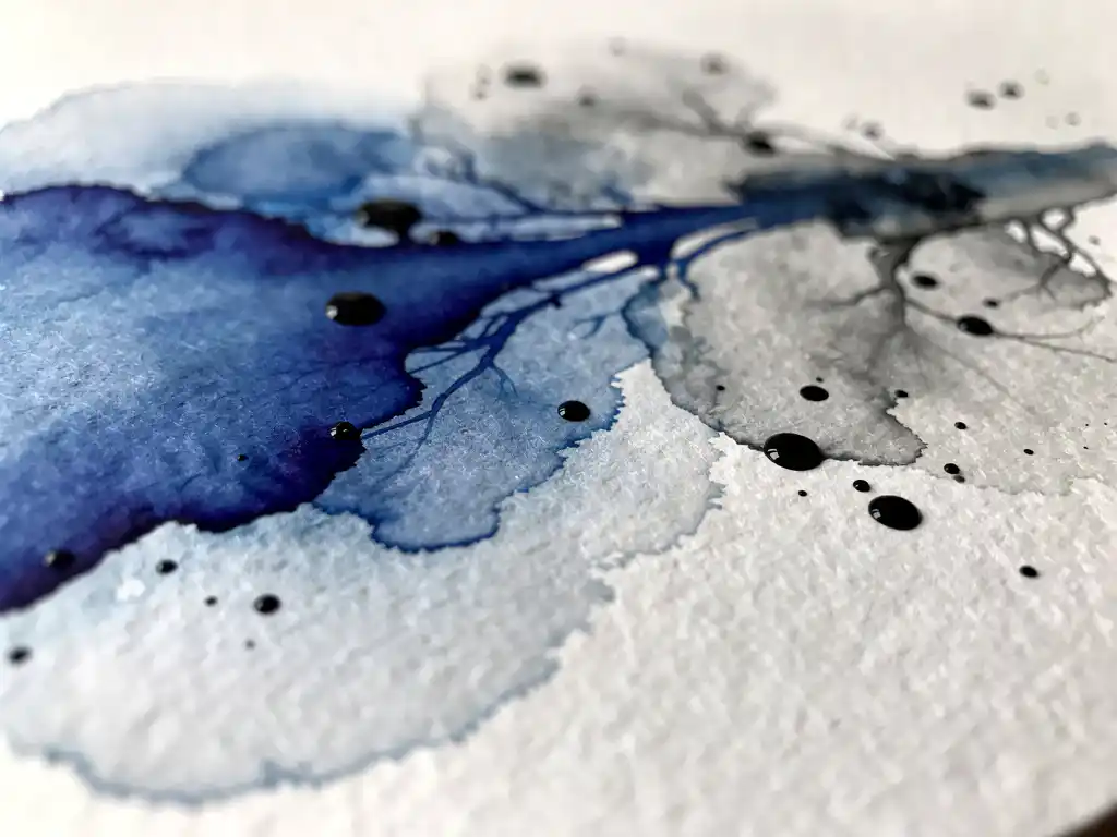 Macro-opname van kobaltblauwe aquarelverf die vloeit over wit papier met natuurlijke textuur en inktvlekken